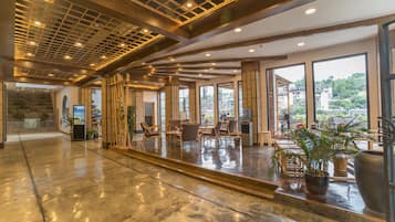 A spacious lobby with a polished concrete floor, large windows offering a view of the city, and a wooden ceiling with recessed lighting.