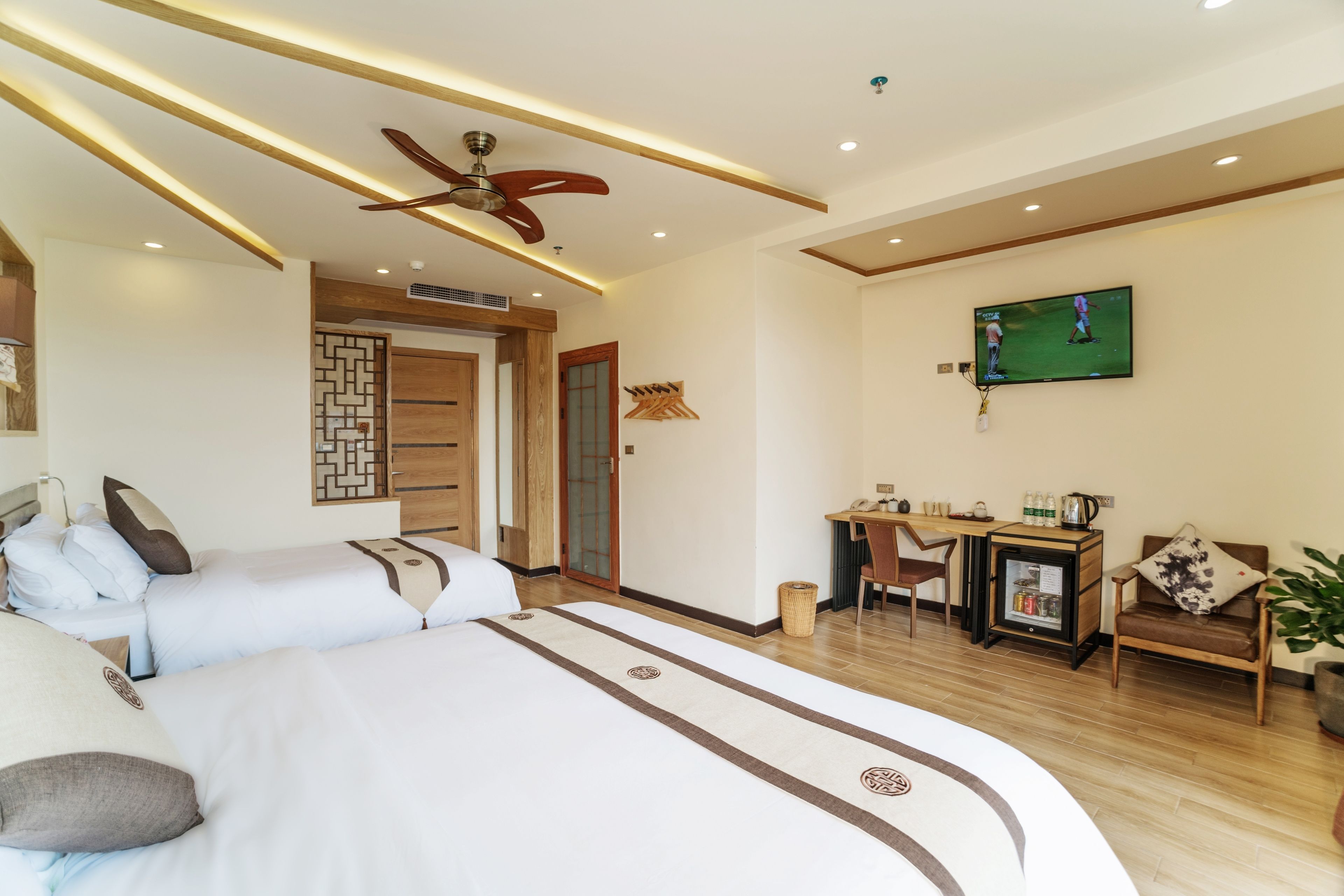 Una habitación de hotel con una cama grande, un escritorio, un televisor y un ventilador de techo.
