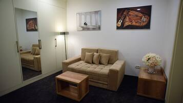 Une pièce avec un canapé beige, une petite table en bois, un miroir et des œuvres d’art accrochées aux murs.