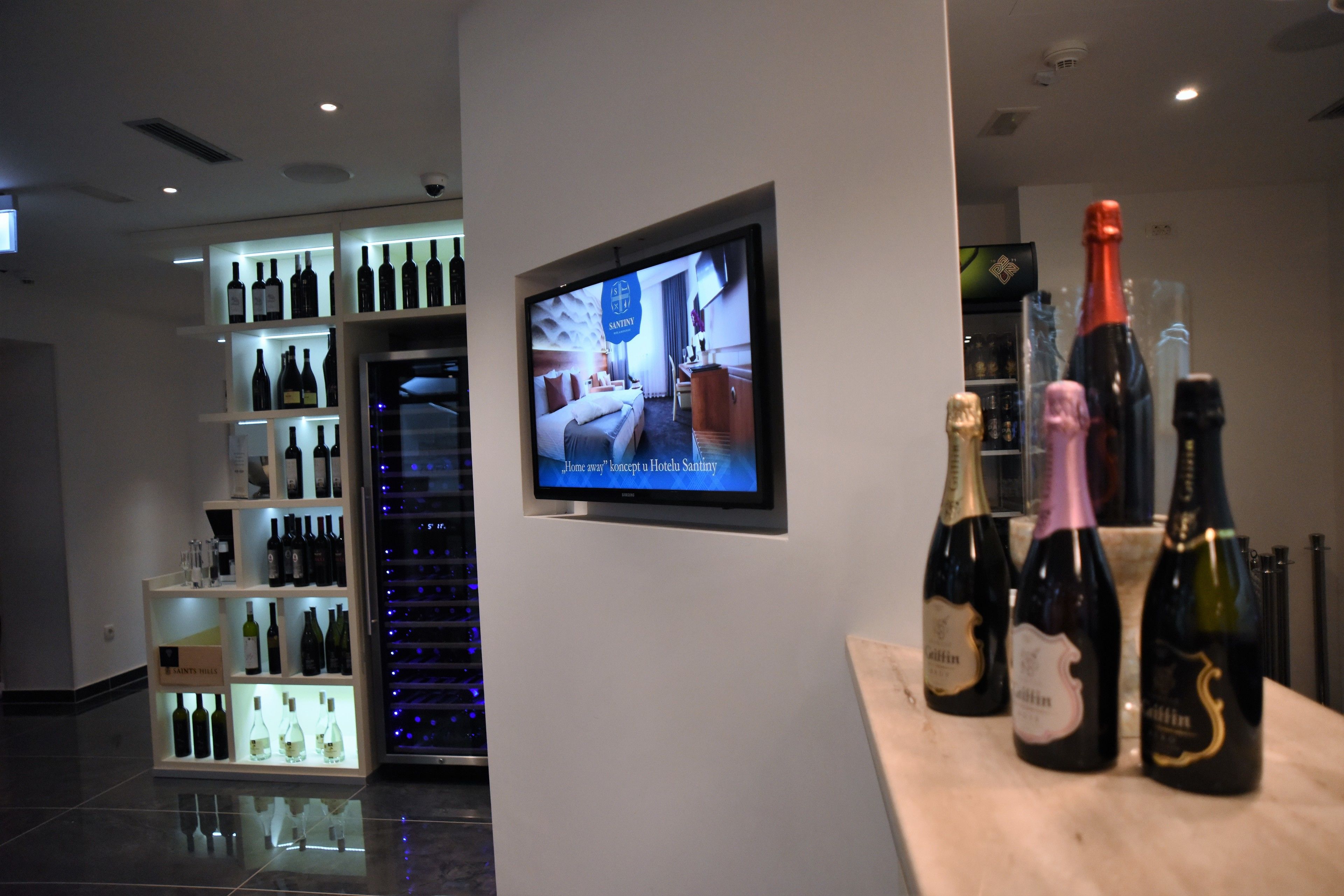 A hotel lobby with a television displaying a room concept, shelves of wine bottles, and a reception desk.