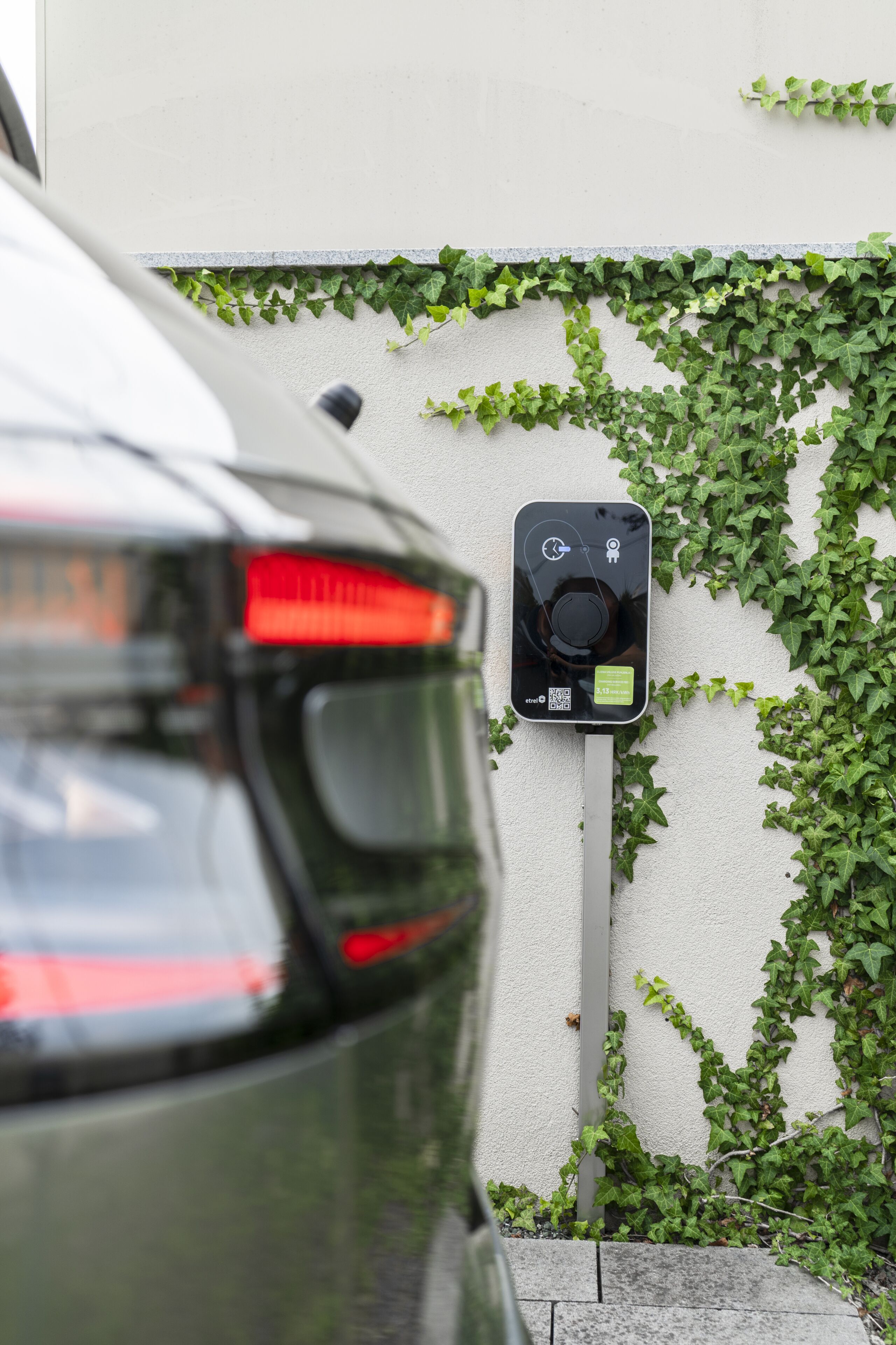 A car parked next to a charging station with a wall covered in ivy.