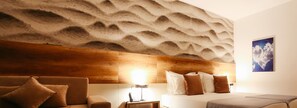 A modern hotel room with a textured wall, a wooden headboard, a bed with white and brown bedding, a bedside table with a lamp, and a framed picture of clouds on the wall. - Santiny Hotel & Restaurant (Sveta Nedelja)