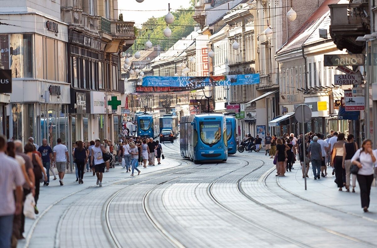 Une rue animée en plein centre-ville, avec des voies de tramway, des piétons et divers commerces.