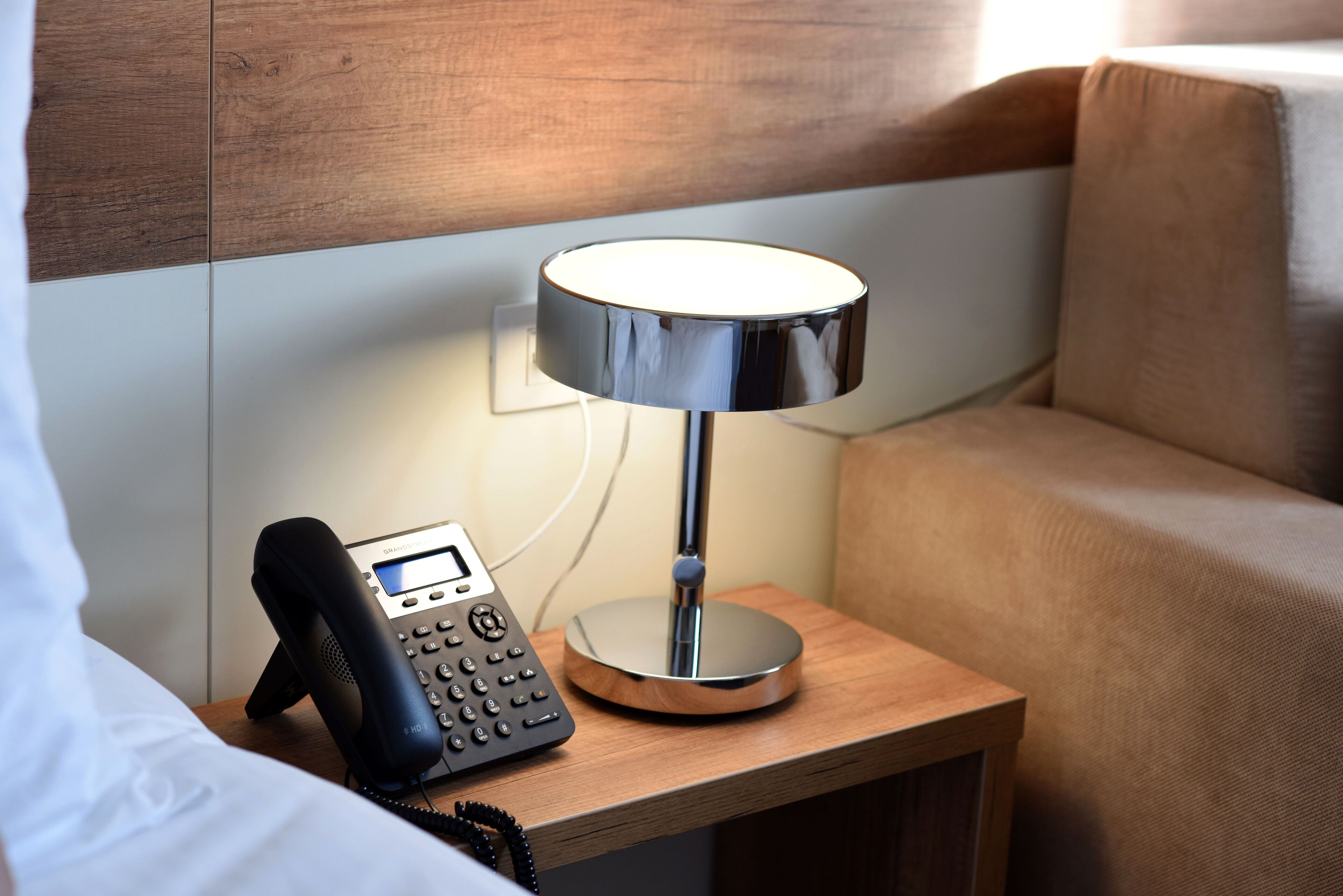 A bedside table with a modern lamp, a telephone, and a power outlet.