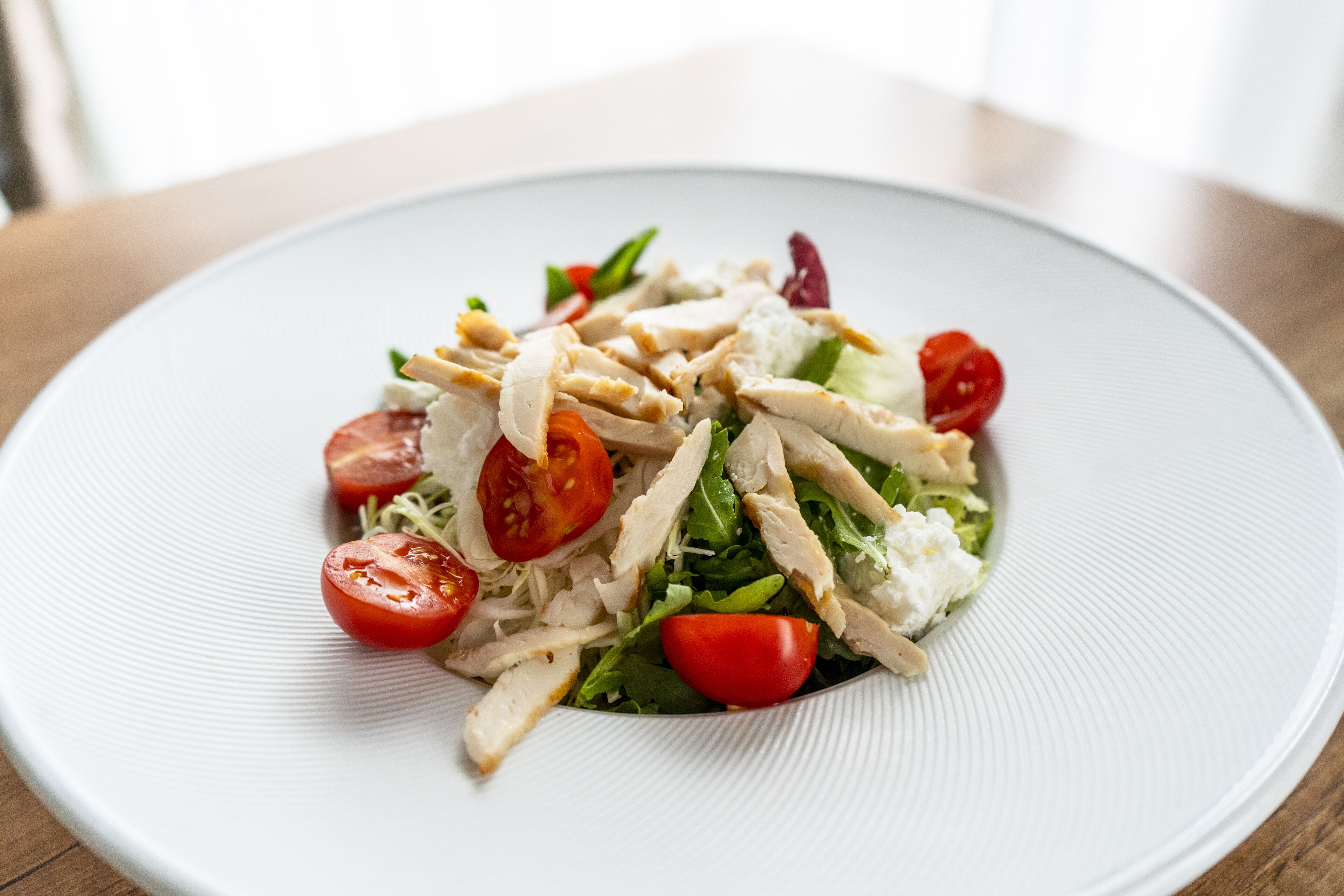 Ensalada con pollo, tomates y verduras de hoja verde.