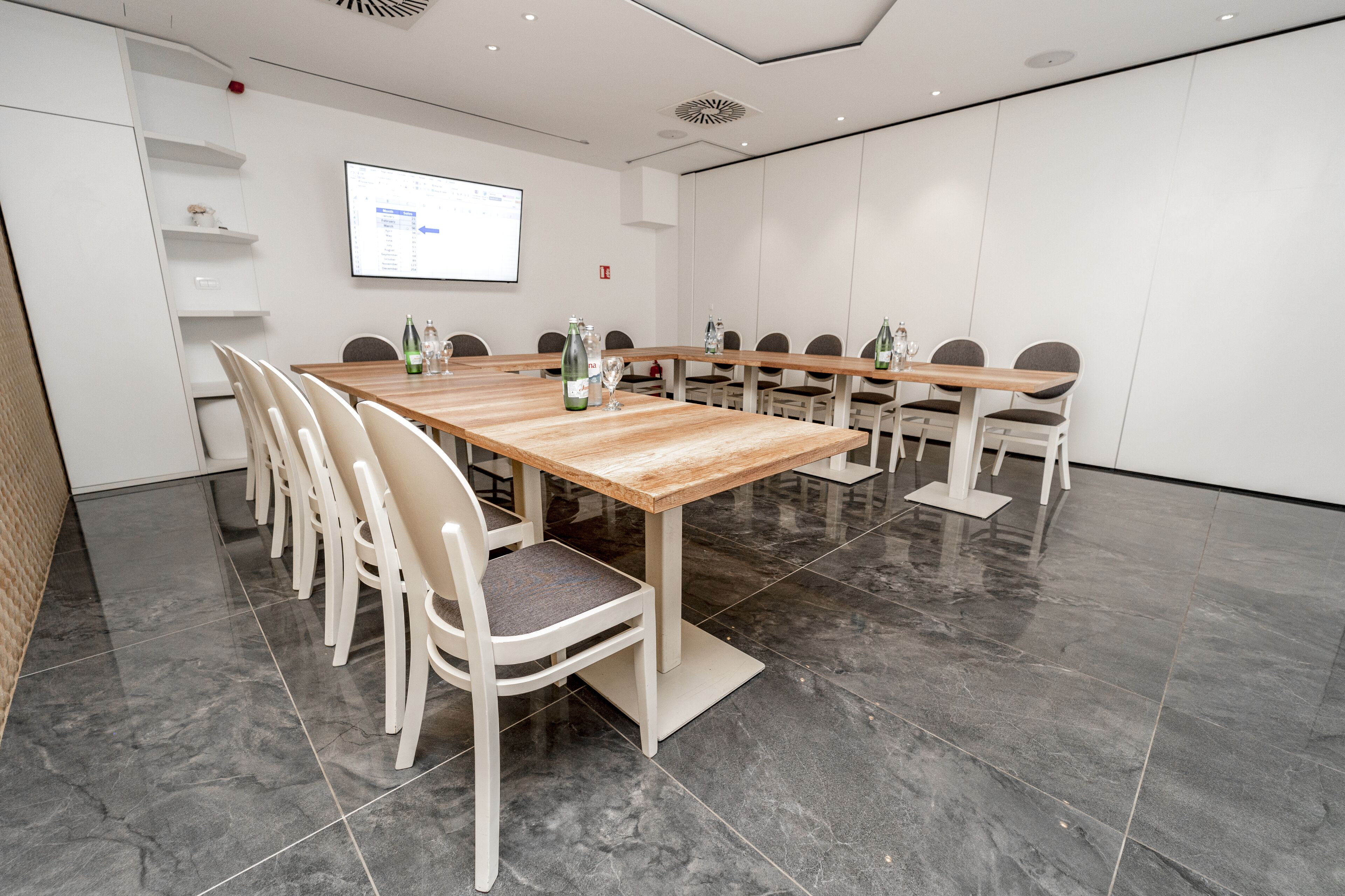 A conference room with a long table, white chairs, and a projector screen.
