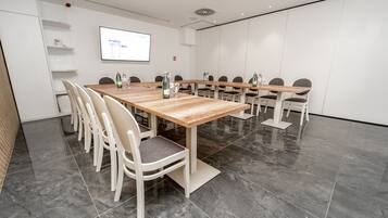 A conference room with a long table, white chairs, and a projector screen.