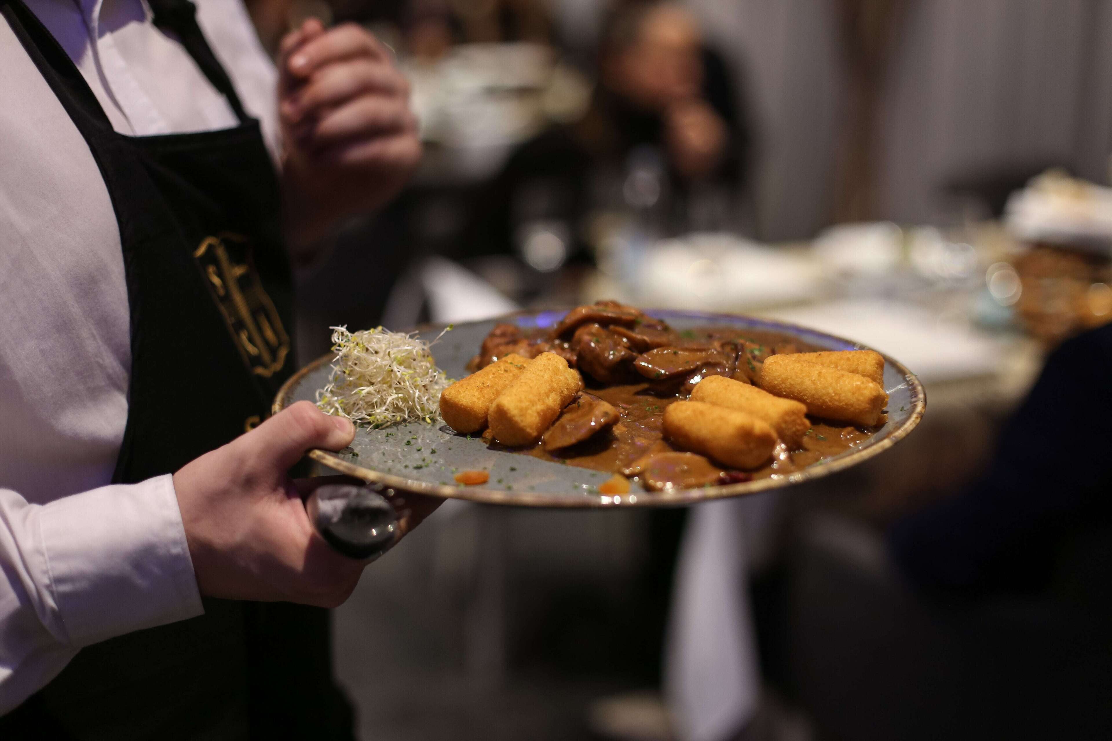 Una persona sostiene un plato con comida, que parece incluir carne y alimentos empanizados, en un ambiente que sugiere un comedor.