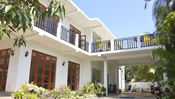 A two-story building with a covered entrance, a balcony with a railing, and a garden area with various plants. - Araliya Blue Beach View Hotel (Negombo)