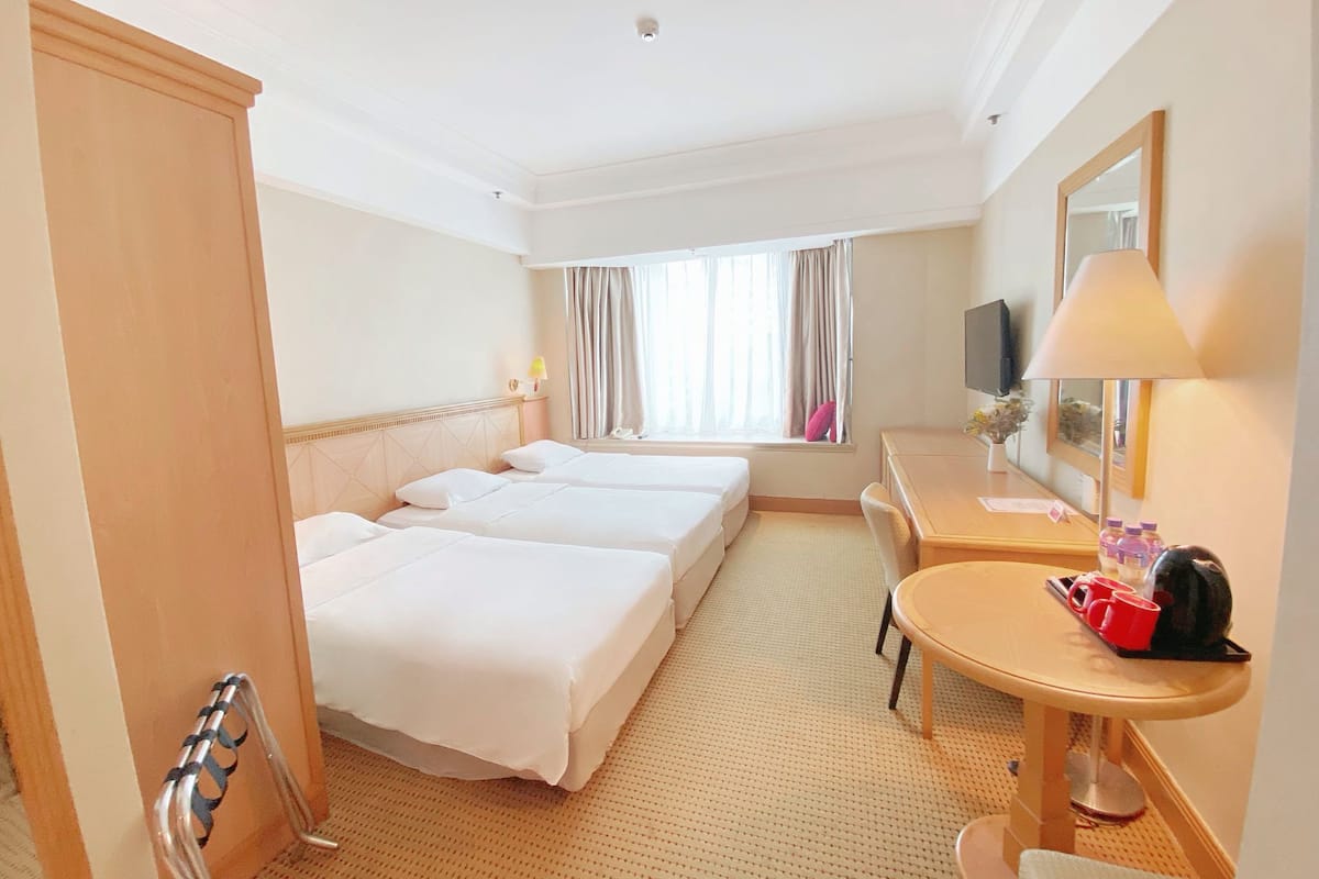 Ein Hotelzimmer mit zwei Betten, einem Schreibtisch mit Stuhl, einem Fernseher und einem Fenster mit Vorhängen.
