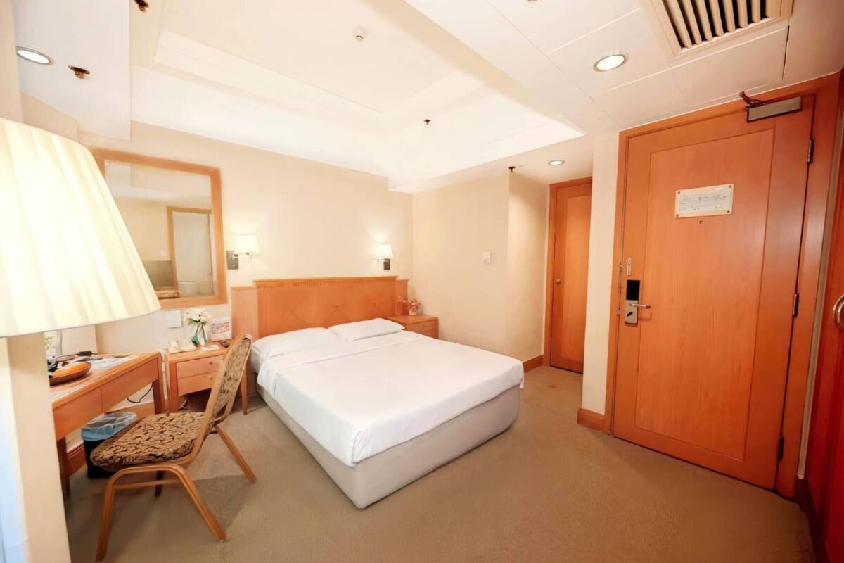 Ein Hotelzimmer mit Bett, Schreibtisch mit Lampe, Stuhl, Kleiderschrank und einer Tür mit einem Schild.
