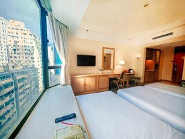 Habitación de hotel con dos camas, un escritorio, una silla, un televisor y un ventanal con cortinas.