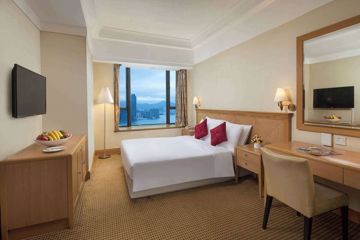 Ein Hotelzimmer mit einem großen Bett, einem Schreibtisch, einem Stuhl, einem Fernseher und Blick auf die Stadt.