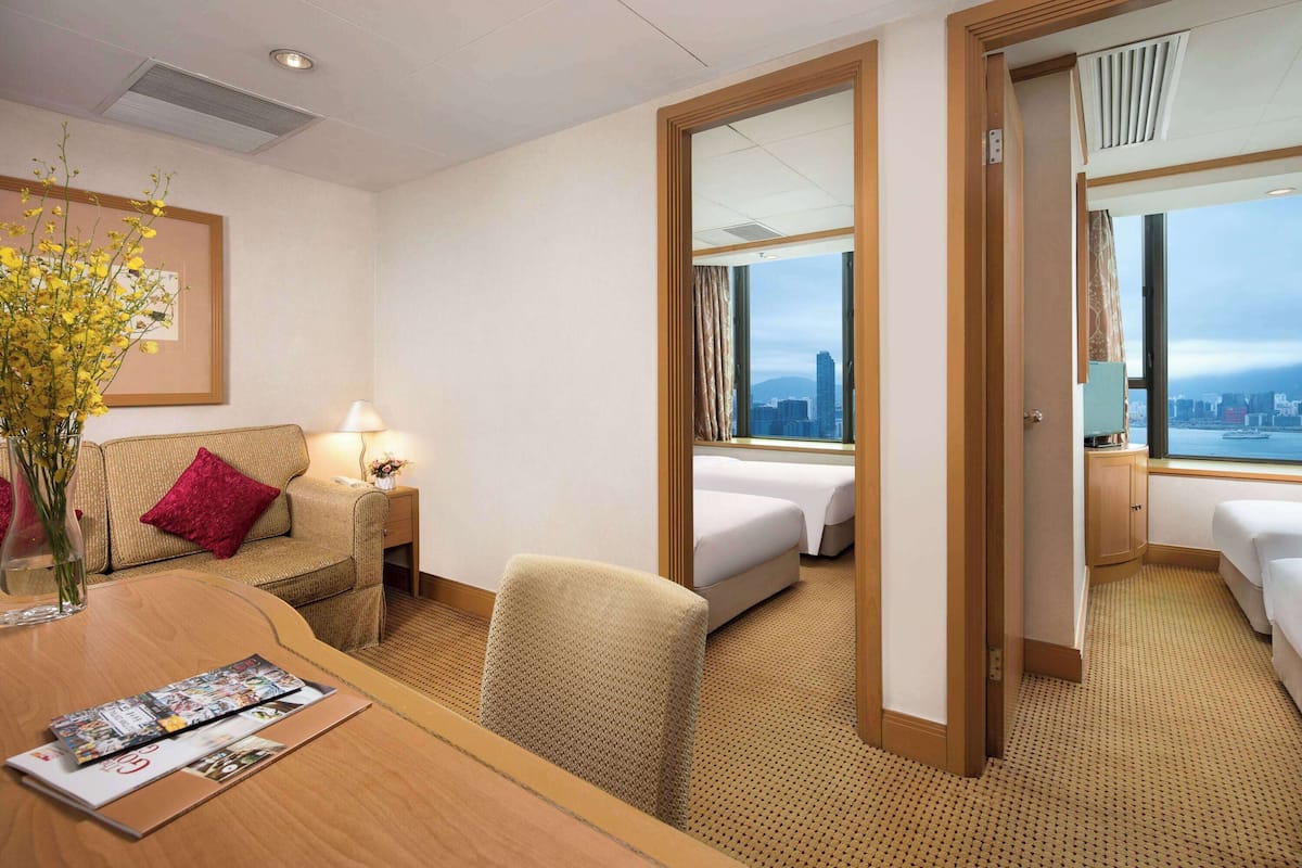Ein Hotelzimmer mit Bett, einer Couch, einem Schreibtisch mit einer Zeitschrift und Blick auf die Stadt durch große Fenster.