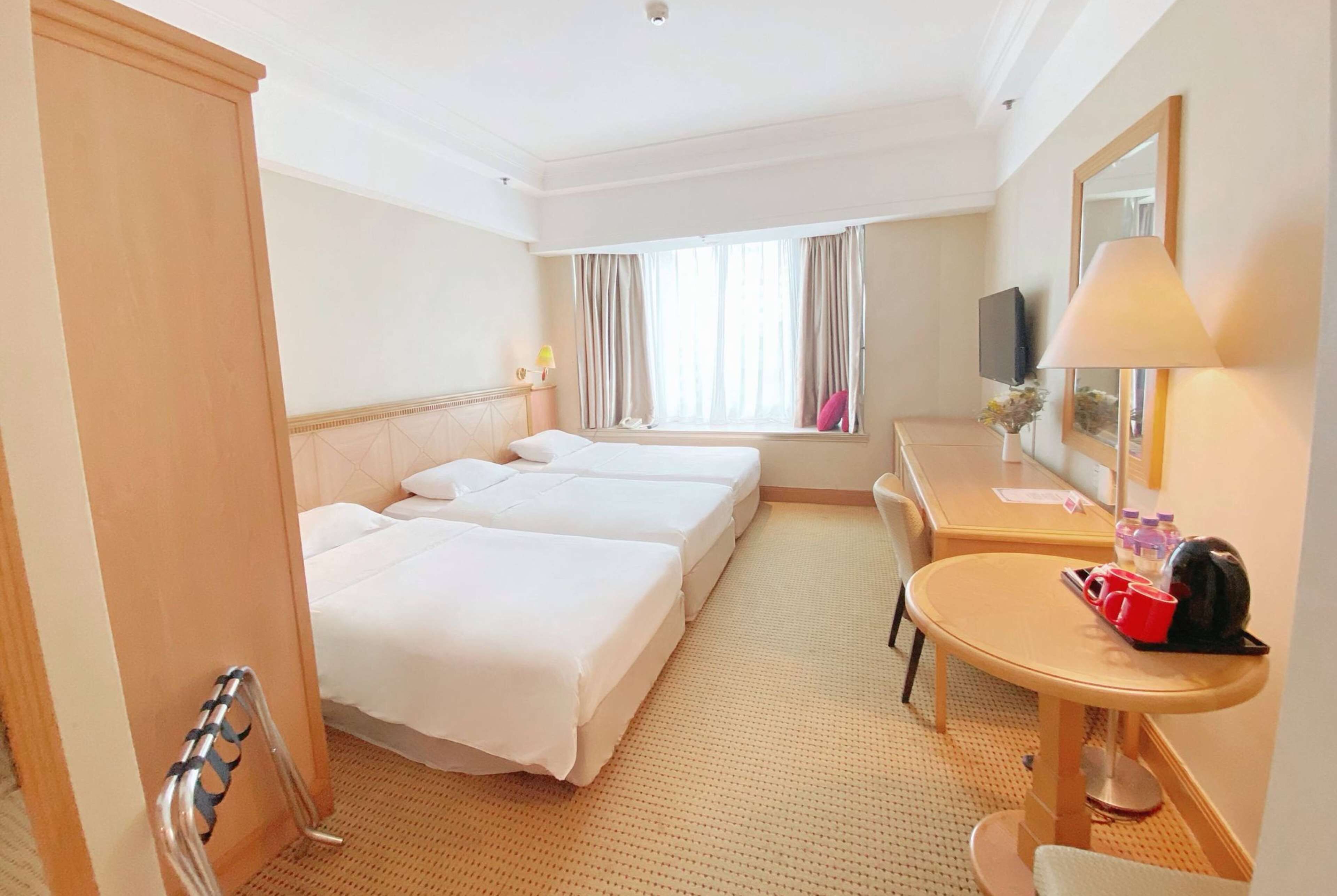 Habitación de hotel con dos camas, un escritorio, una silla, un televisor y una ventana con cortinas.