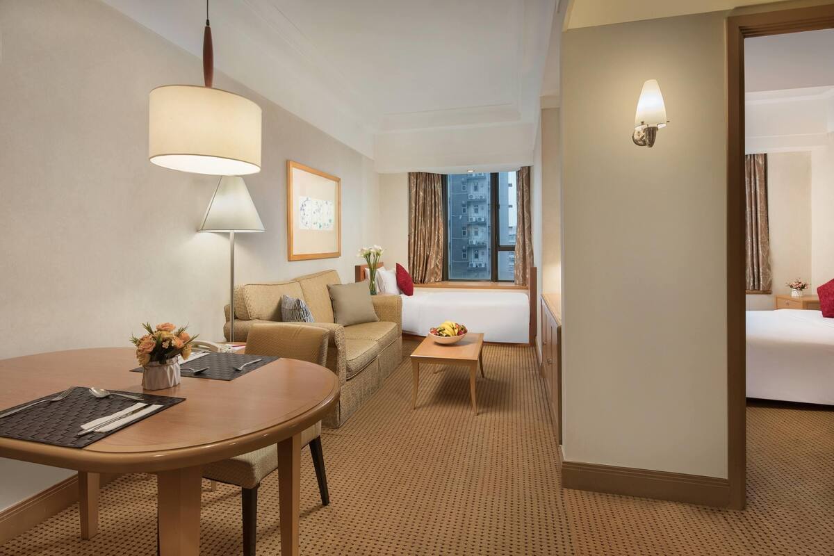 Ein Hotelzimmer mit Essbereich, einer Couch, einem Bett und einem Fenster mit Vorhängen.