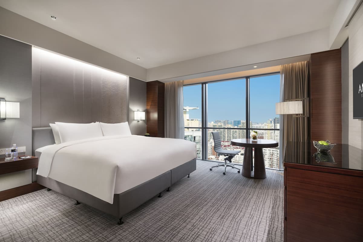A modern hotel room with a large bed, a desk, a chair, and a view of the city.