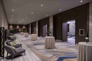 A spacious hotel lobby with a long, patterned carpet, several round tables, and comfortable seating areas.