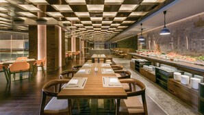 A modern restaurant with a long counter, wooden tables, and chairs.