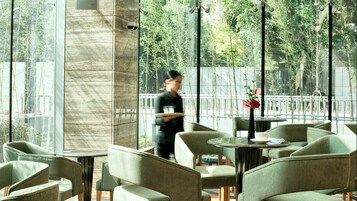 A restaurant with outdoor seating, large windows, and a view of trees.