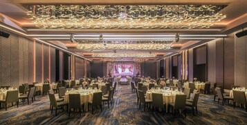A banquet hall with round tables, chairs, and a stage at the far end.