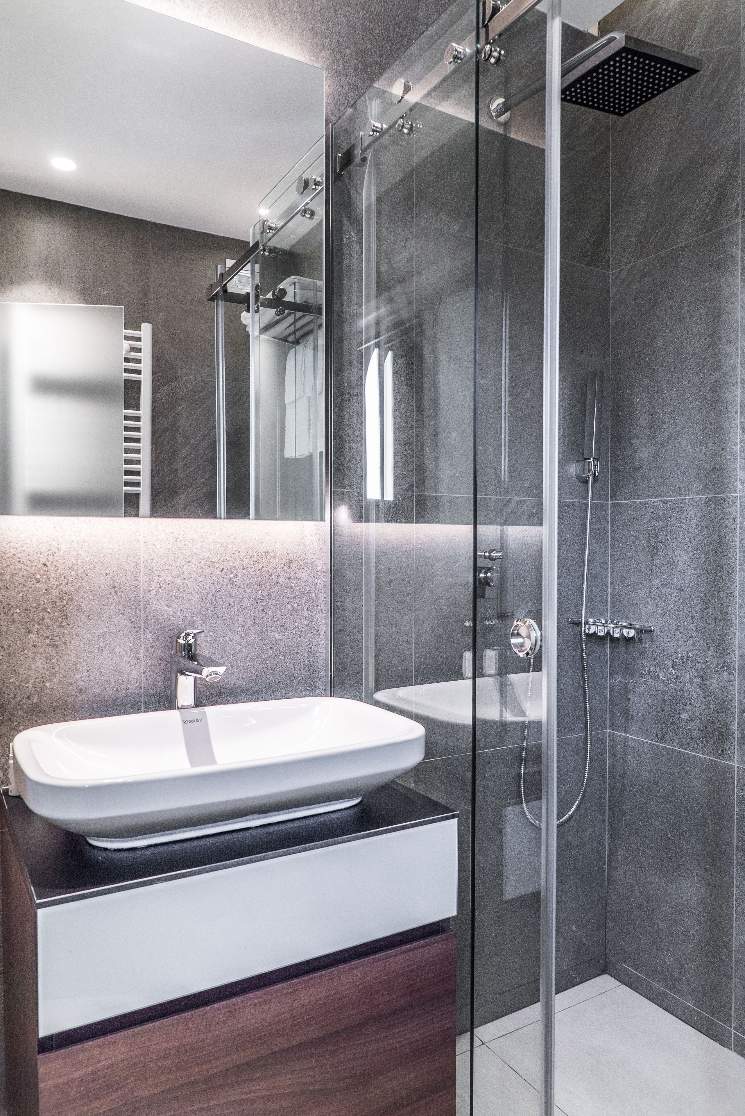 Un baño moderno con ducha de vidrio, un lavabo blanco y un espejo sobre el lavabo.