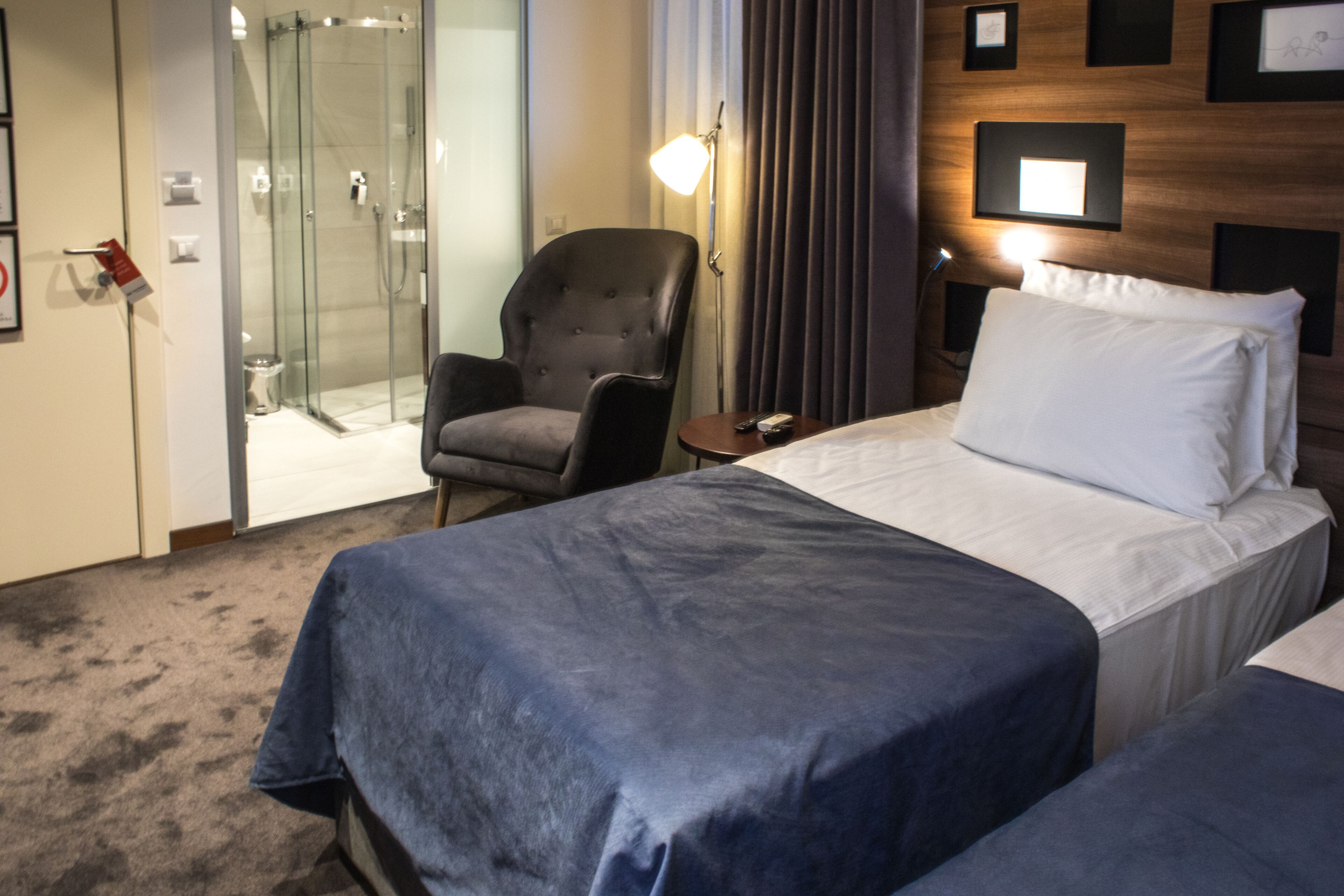 A hotel room with a bed, a chair, a small table, and a shower area.
