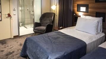 A hotel room with a bed, a chair, a small table, and a shower area.