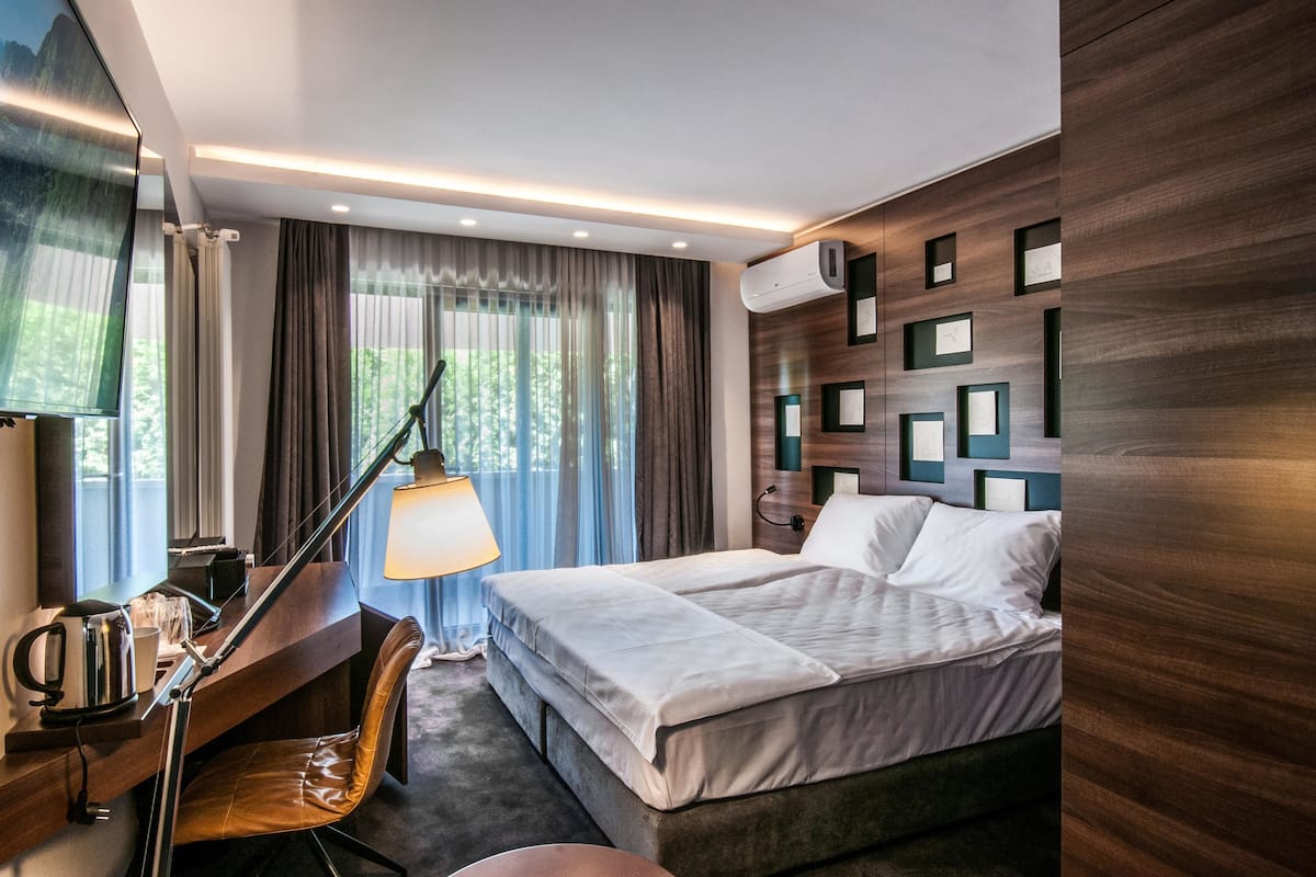 Une chambre d’hôtel équipée d’un lit, d’un bureau, d’une chaise, d’une lampe et d’un climatiseur fixé au mur.