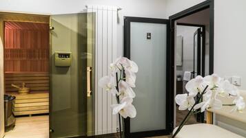 A modern bathroom with a glass shower enclosure, a wooden sauna, and white orchids.