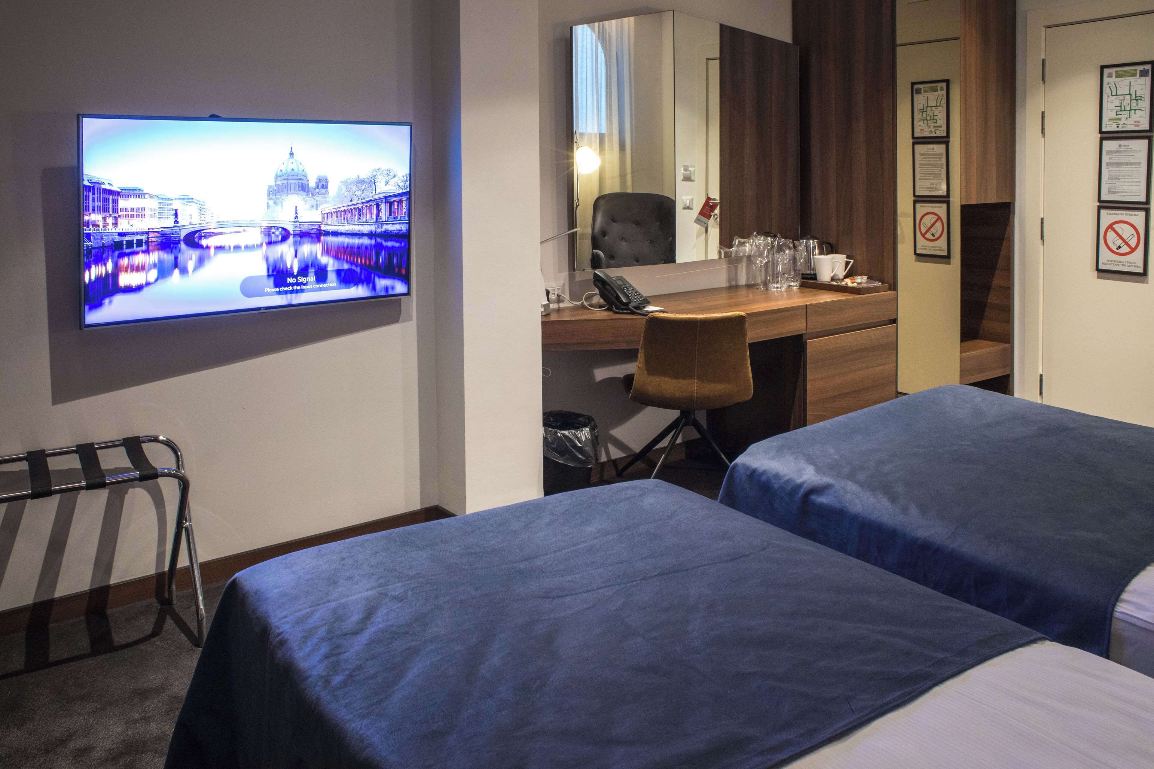 A hotel room with two beds, a desk, a chair, a TV, and a mirror.