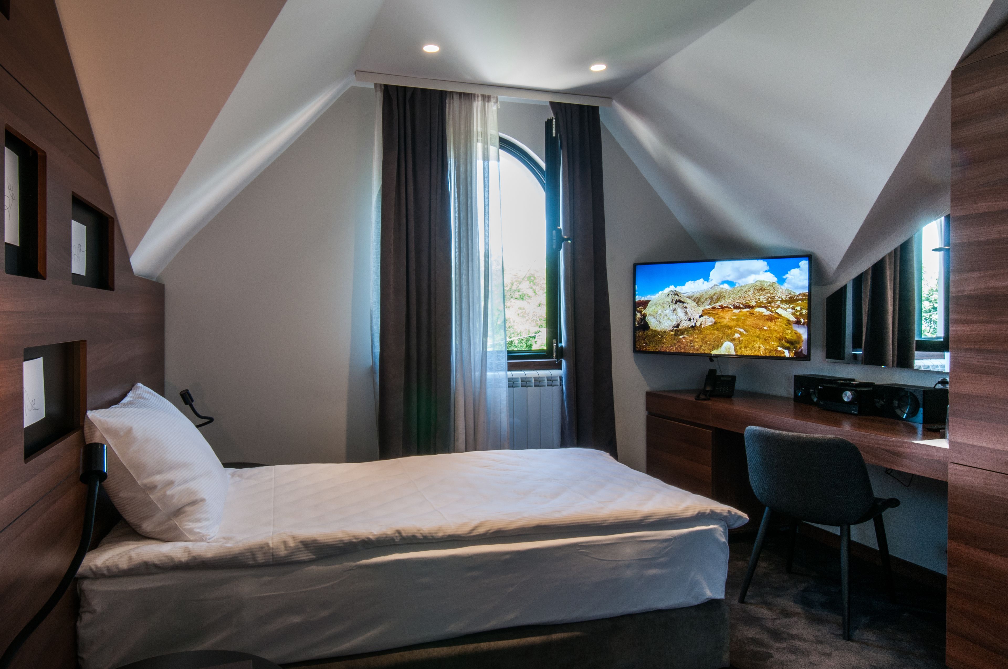 A modern hotel room with a bed, desk, and TV.