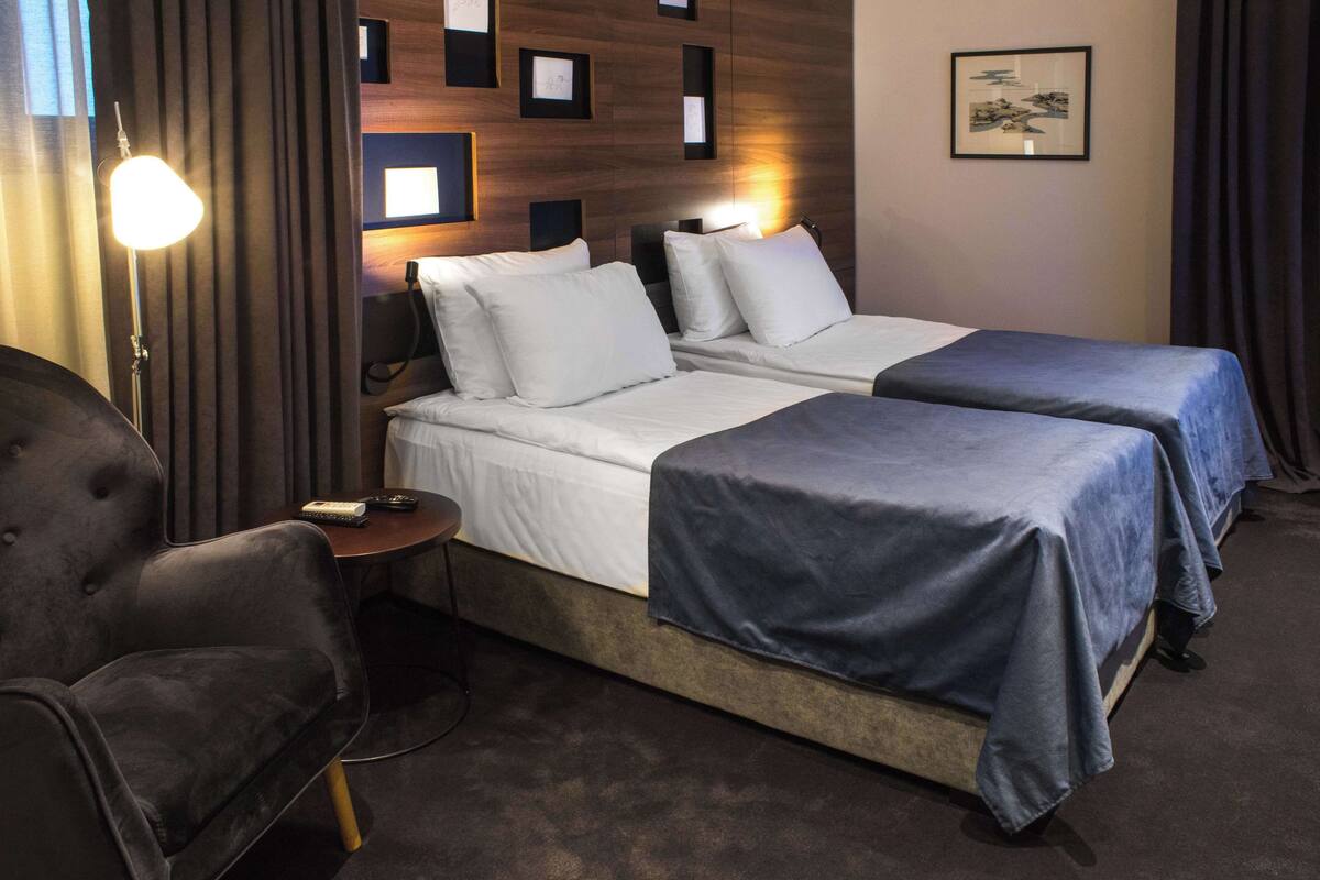 Une chambre d’hôtel avec deux lits, un bureau, une chaise et une lampe.