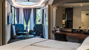 Quarto de hotel com uma cama, uma escrivaninha com computador, uma cadeira e uma televisão na parede.