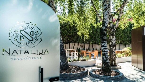Uma área externa moderna com o logotipo 'Natalija Residence' e um espaço de refeições com mesas e cadeiras.