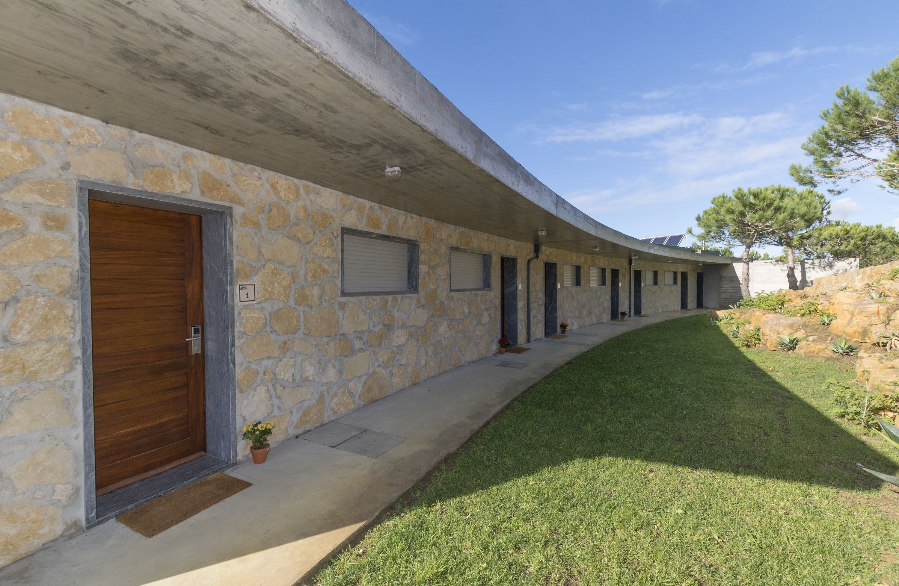 Un bâtiment moderne doté d’un toit incurvé, de murs en pierre et d’une pelouse bien entretenue.