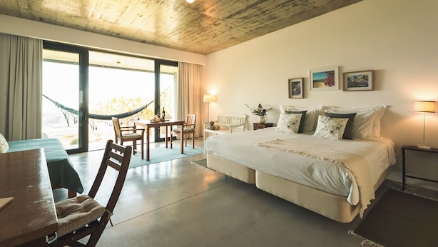 A spacious bedroom with a large bed, a dining area with a table and chairs, and a hammock by the window.