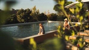 A pool area with a person sitting on the edge and another person sitting on a bench.