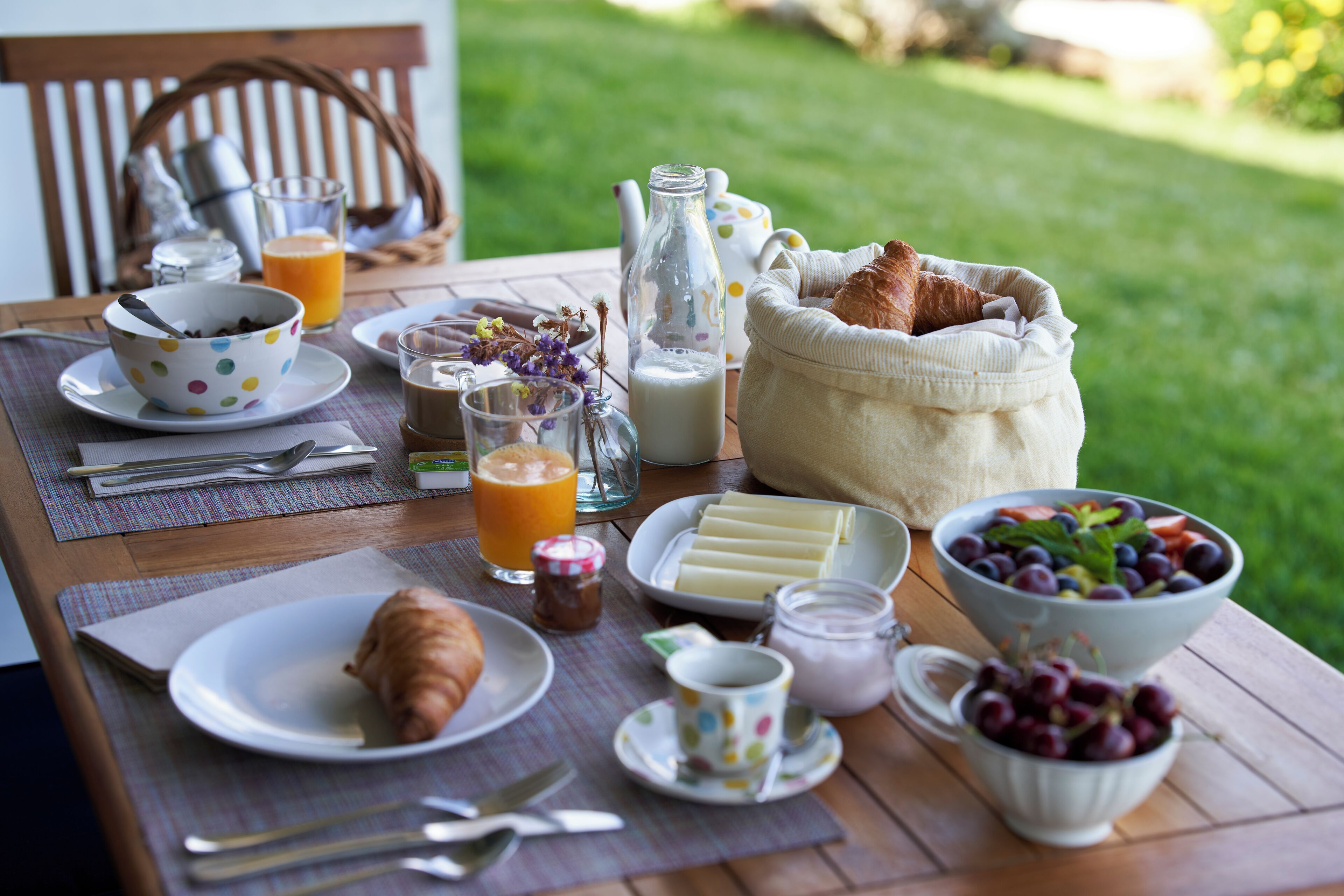A breakfast table with croissants, cheese, fruit, and beverages.