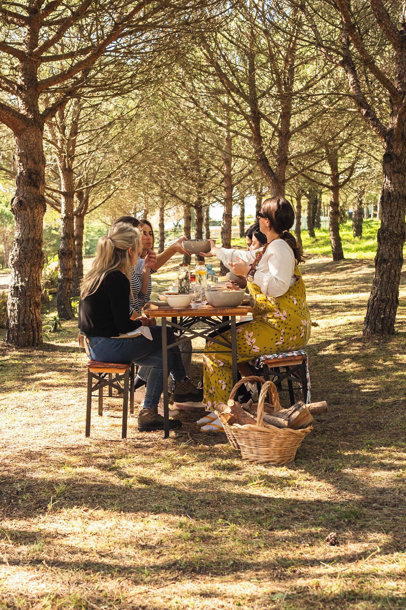 Un grupo de personas sentadas en una mesa de madera al aire libre, rodeadas de árboles.