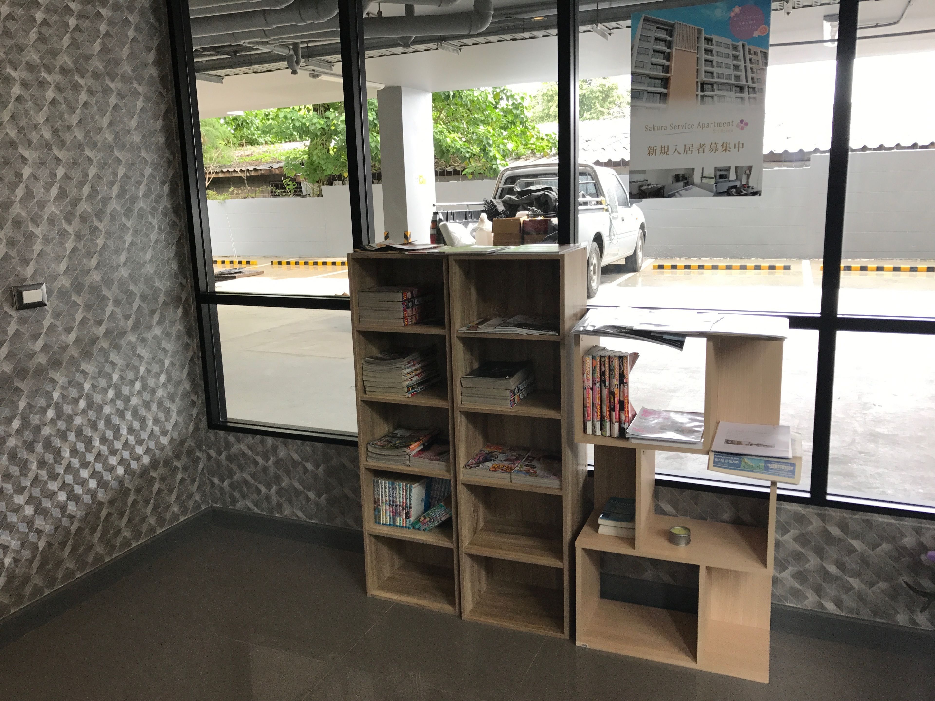 A room with a large window, a wooden bookshelf, and a small desk with a computer.
