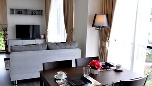 Quarto de hotel moderno com sofá cinza, mesa de jantar posta com uma chávena, um copo e um vaso de flores.