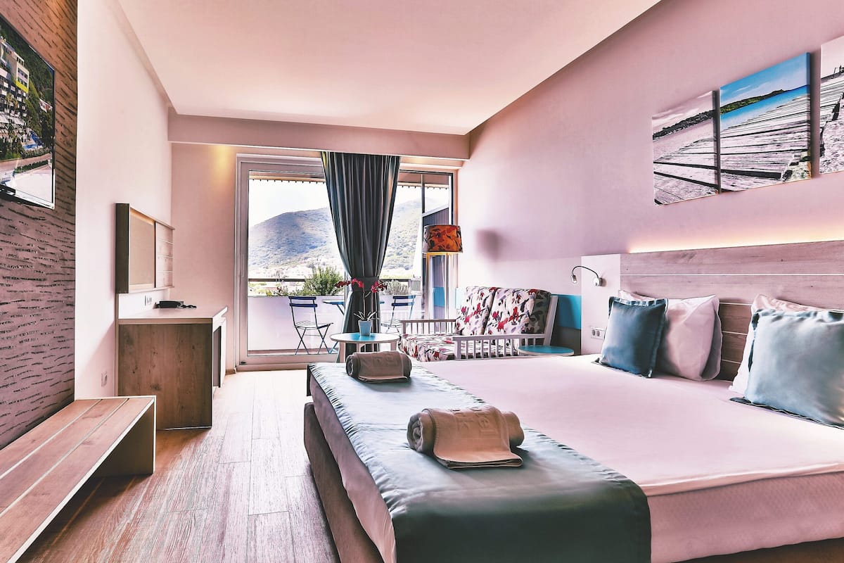 Una habitación de hotel moderna con una cama grande, un escritorio y un balcón con vistas a las montañas.