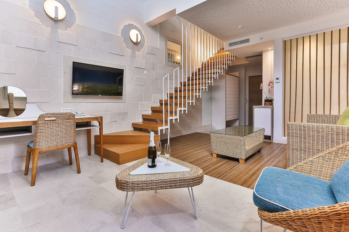 Una sala de estar moderna con una escalera, un televisor de pantalla plana, muebles de mimbre y un comedor.
