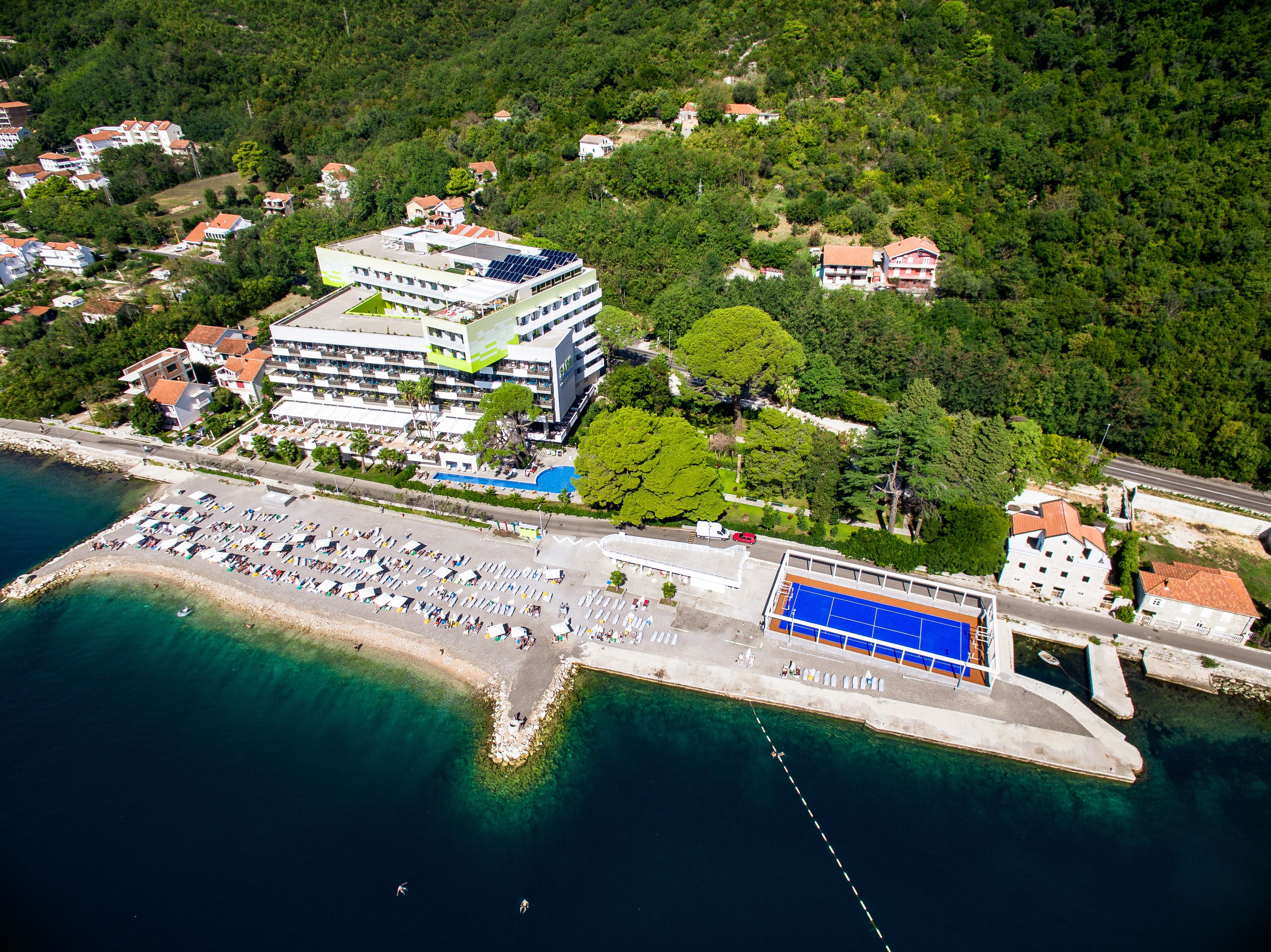 Vista aérea de una zona costera con un gran complejo hotelero, un puerto deportivo y una playa con numerosas tumbonas.