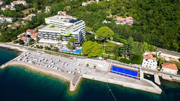 Vista aérea de una zona costera con un gran complejo hotelero, un puerto deportivo y una playa con numerosas tumbonas.
