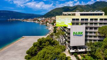 Un hotel con un llamativo letrero que dice 'PARK HOTEL', situado cerca de una zona costera con playa y montañas al fondo.