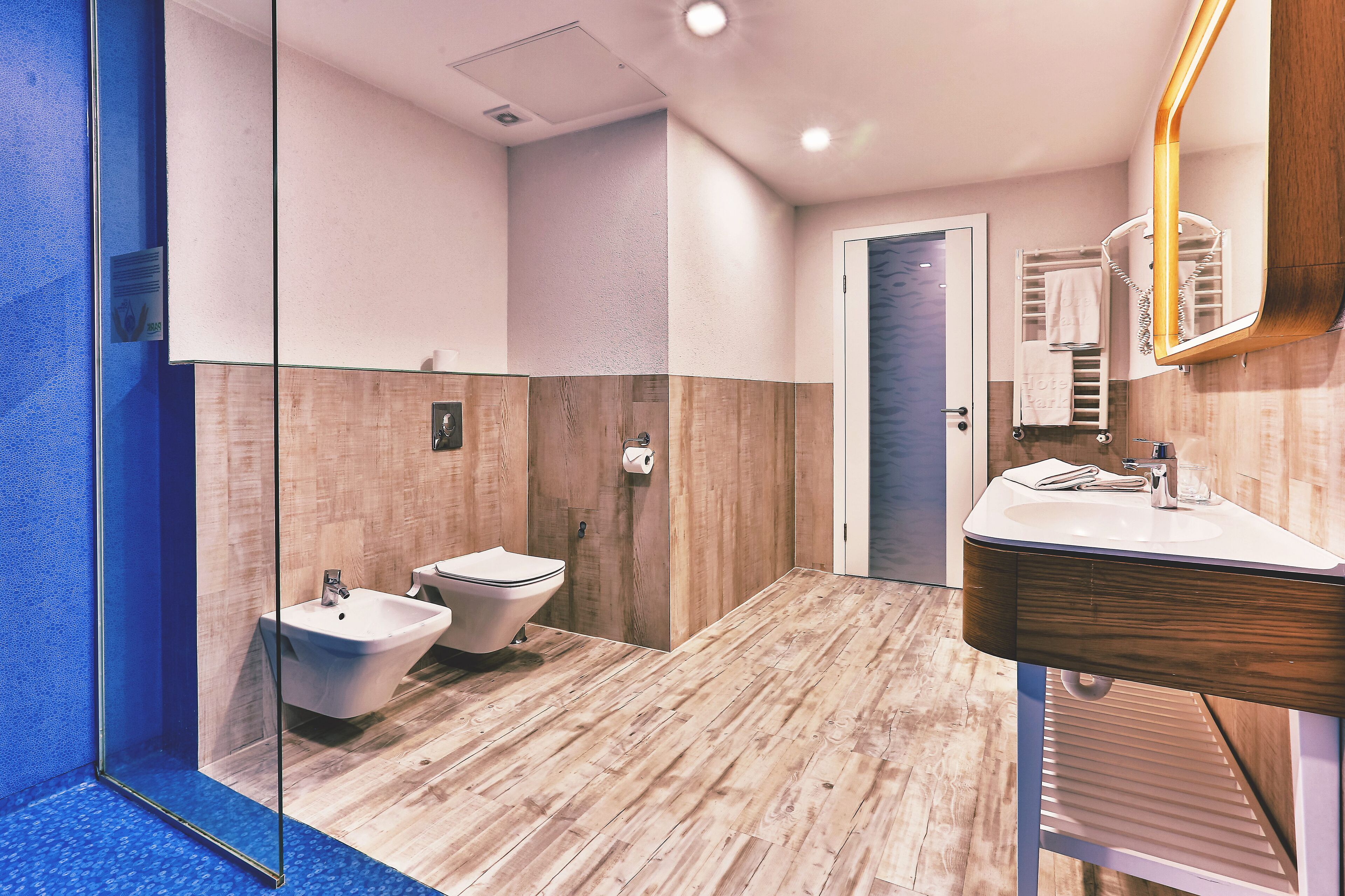Een moderne badkamer met een douchecabine van glas, een houten wastafelmeubel met spiegel en twee toiletten.