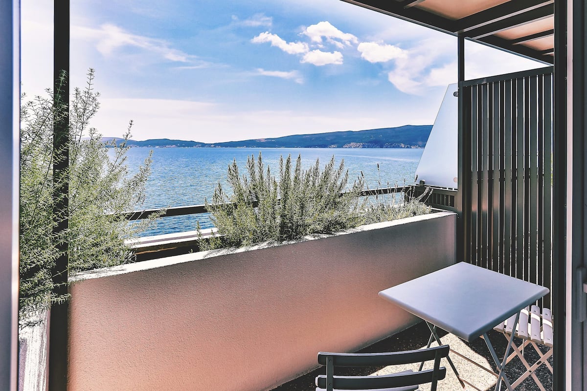 Un balcón con vista a un lago y montañas, una mesa y sillas.