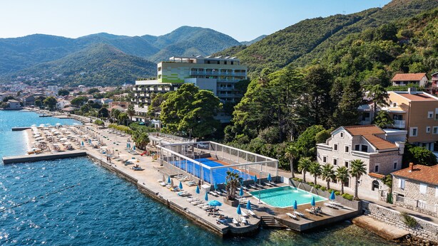 Een hotel aan de kust met een zwembad, een lounge aan het strand en uitzicht op bergen.